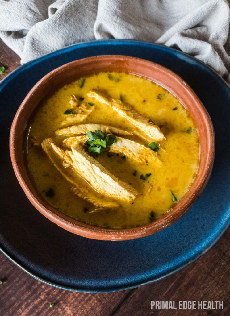 Bowl of yellow soup on a blue place on wooden surface.