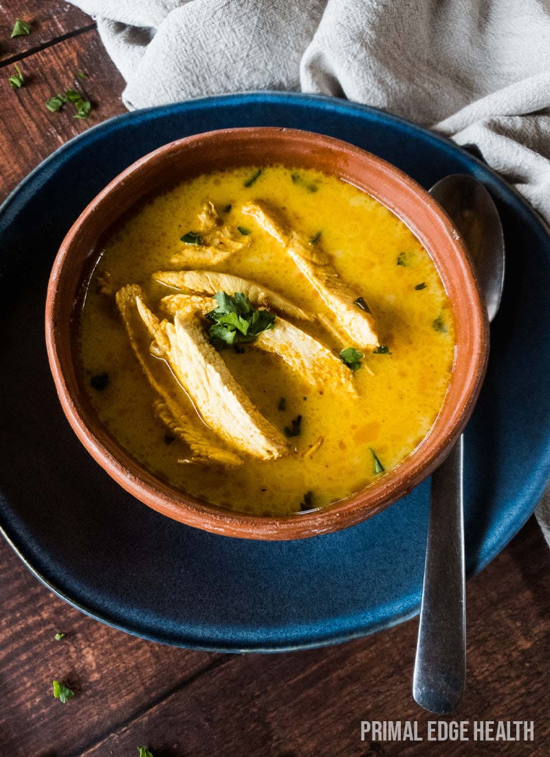 Yellow soup with meat in a bowl with spoon on blue plate.