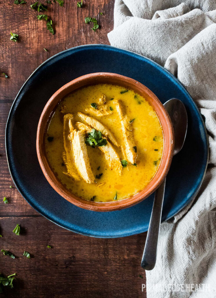 Bowl of yellow soup on a wooden surface with spoon and white cloth.