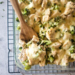 A glass container of chicken broccoli casserole in with a wooden spoon.