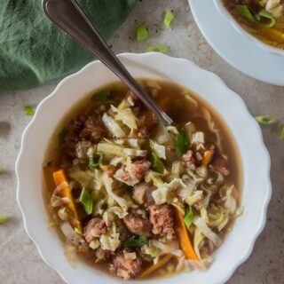 A bowl of soup with meat and vegetables, served with a spoon.