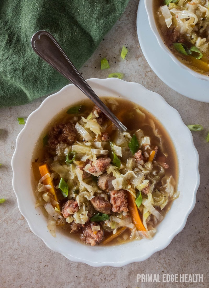 A bowl of soup with meat and vegetables, served with a spoon.