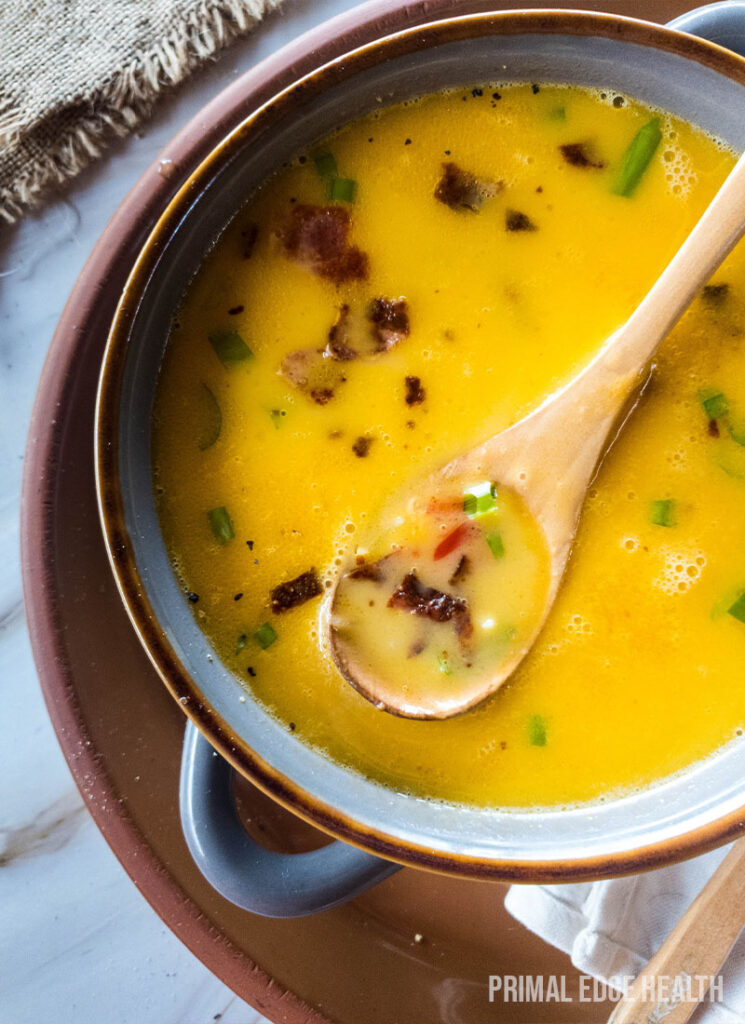 A bowl of beer cheese soup garnished with bacon and herbs, served with a wooden spoon.