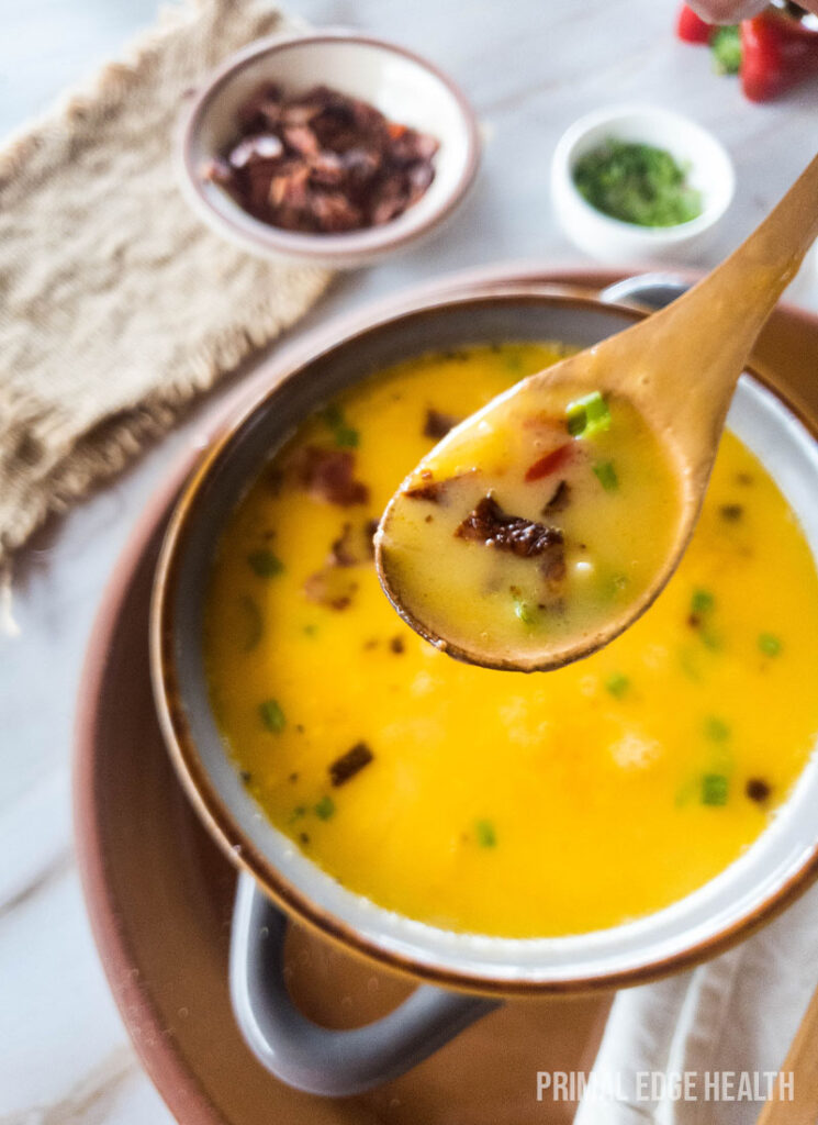 A wooden spoon serving a keto beer cheese soup garnished with herbs.