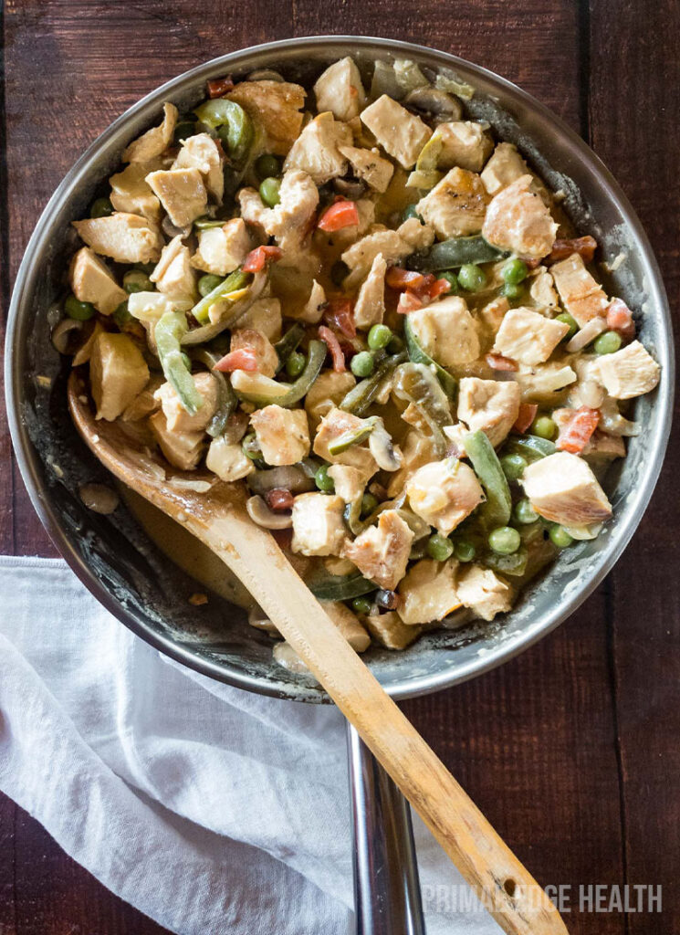 keto chicken a la king in a skillet on a wooden table with a wooden spoon.