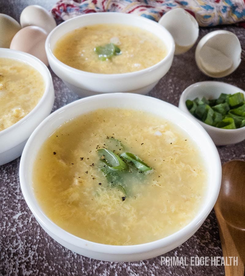Three bowls of egg drop soup, with garnish on a grey surface.