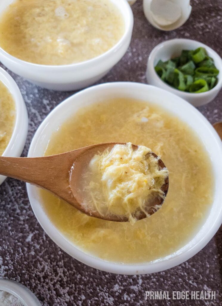 A bowl of egg drop soup, with a wooden spoon.