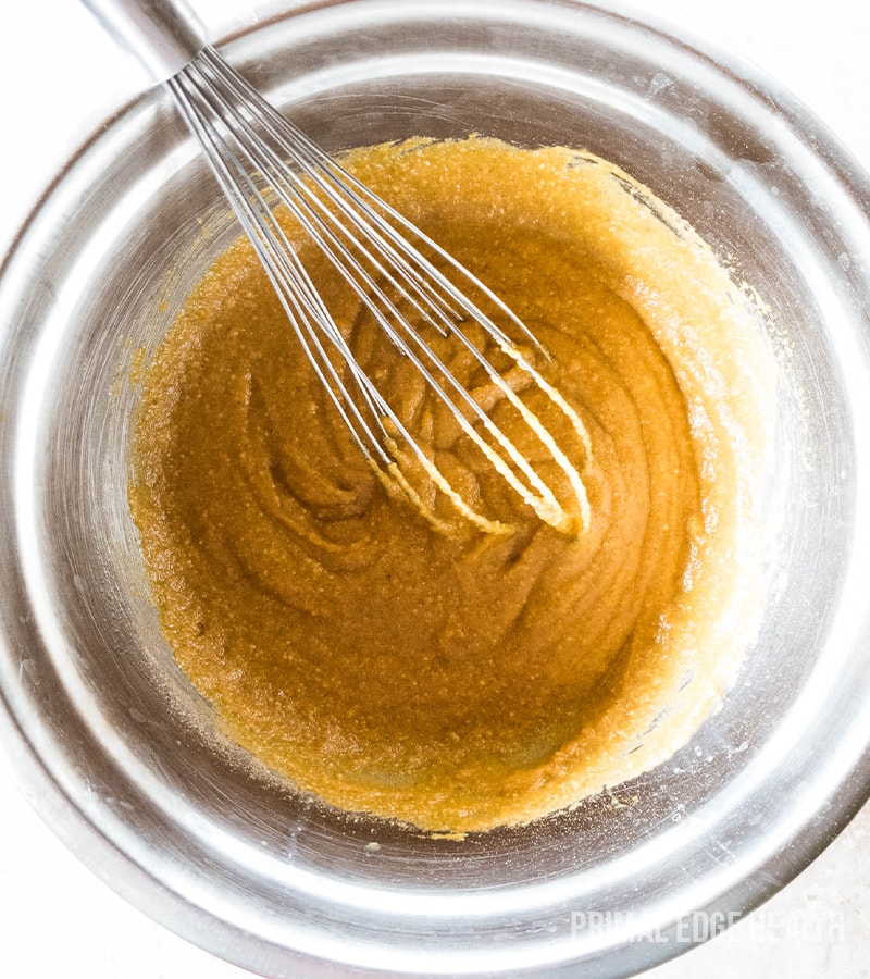 Mixing pumpkin muffin batter in a stainless steel bowl with a wire whisk.