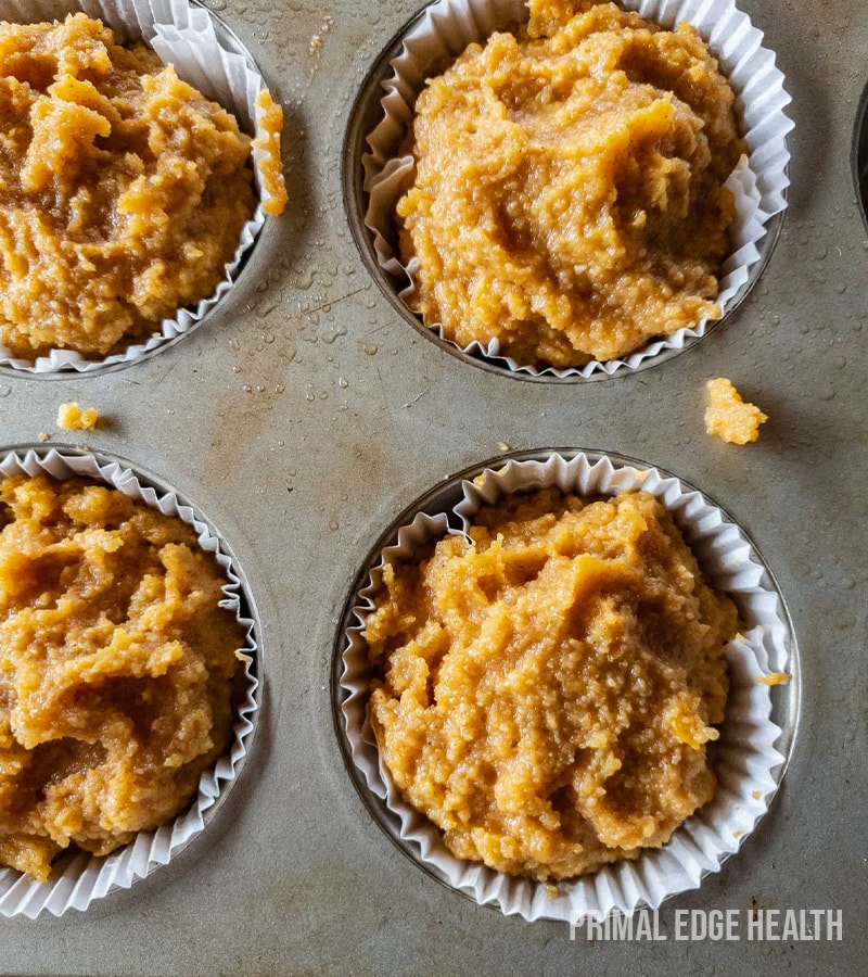 Pumpkin muffin batter portioned into paper liners on a tray.