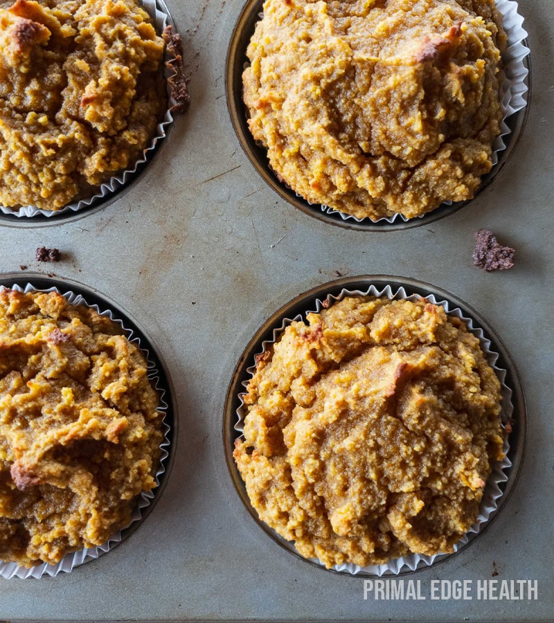 Four pumpkin muffins in a muffin tin on a grey surface.