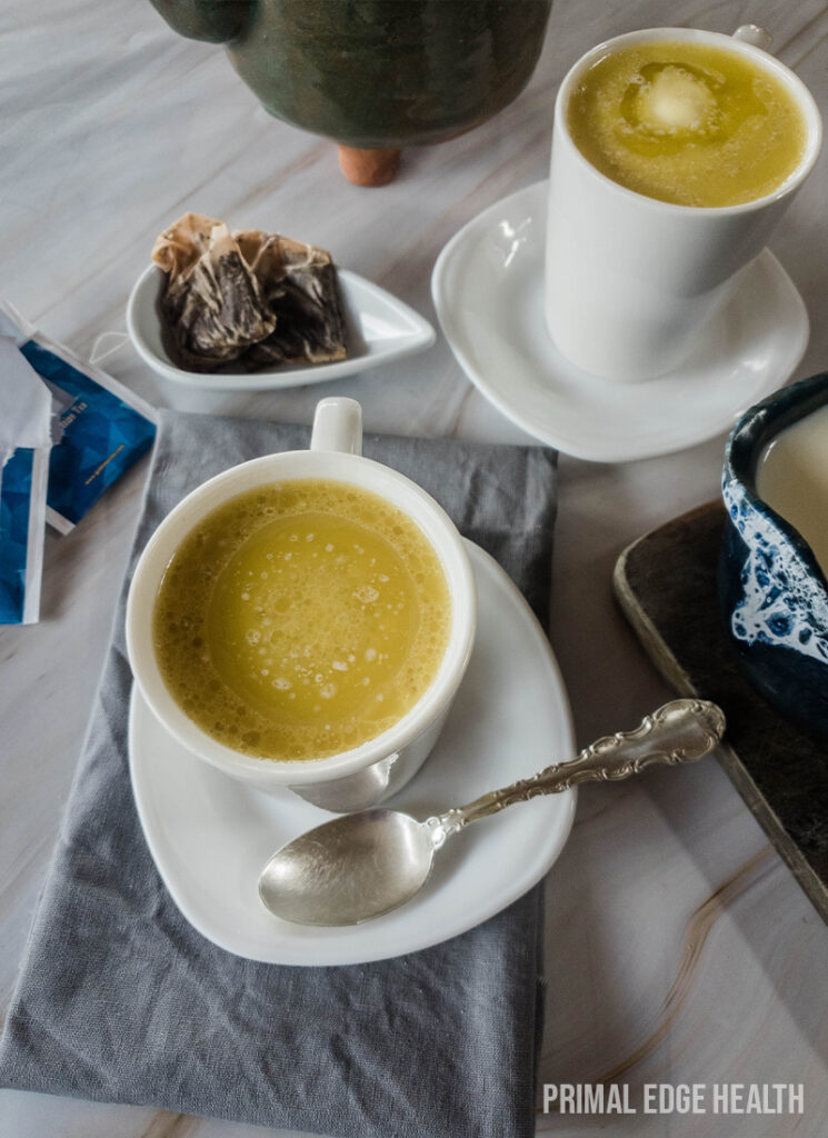 A cup of butter tea served with a spoon on a saucer, on a white surface.
