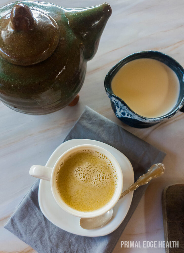 A cup of butter tea with a spoon, next to a creamer.