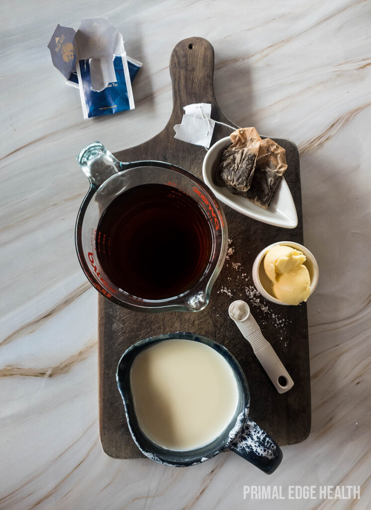 Various ingredients on a wooden cutting board including a jug of butter tea, butter, and a bowl of cream.