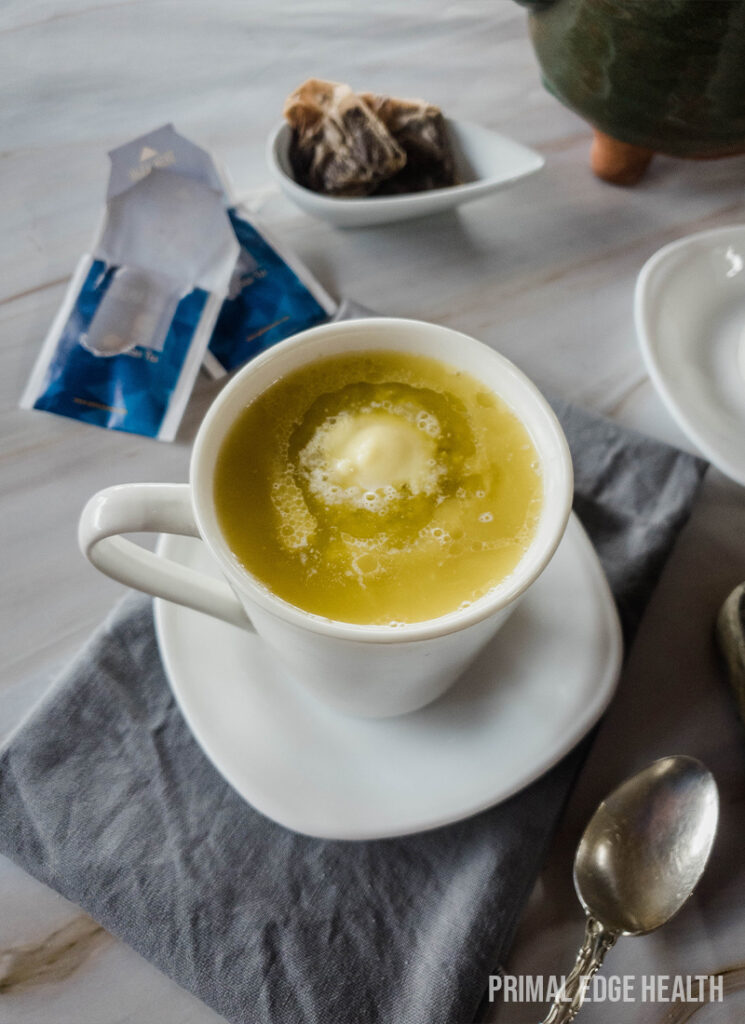 A cup of yellow liquid on a marble surface with tea bags.