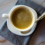 A cup of tea on a saucer with a spoon, resting on a grey napkin.