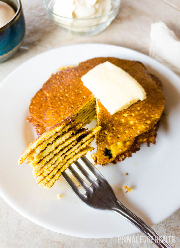 A stack of pancakes topped with a pat of butter on a plate with a fork.