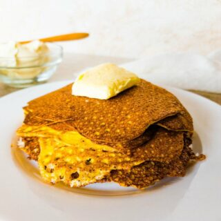 A stack of pancakes with a pat of butter on top on a plate.