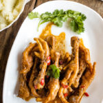 Chicken feet adobo served with garnish on a white place on wooden surface.