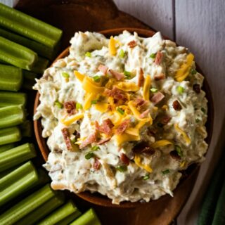 Bowl of creamy crack dip served with celery sticks on a wooden platter.