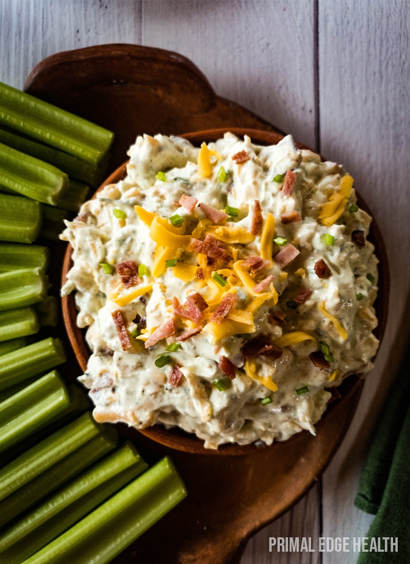 Bowl of creamy crack dip served with celery sticks on a wooden platter.