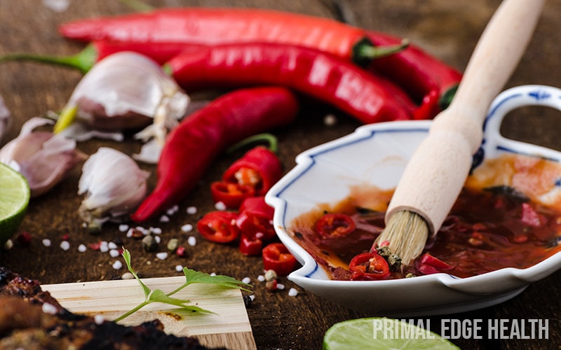 Various spices and a brush dipped in red sauce on a wooden surface.