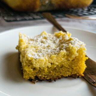 A piece of keto gooey butter cake on a white plate with a fork on the side.