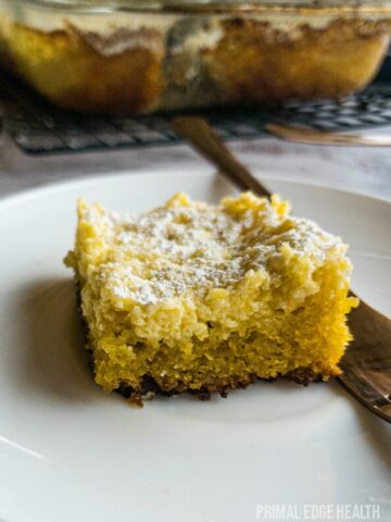 A piece of keto gooey butter cake on a white plate with a fork on the side.