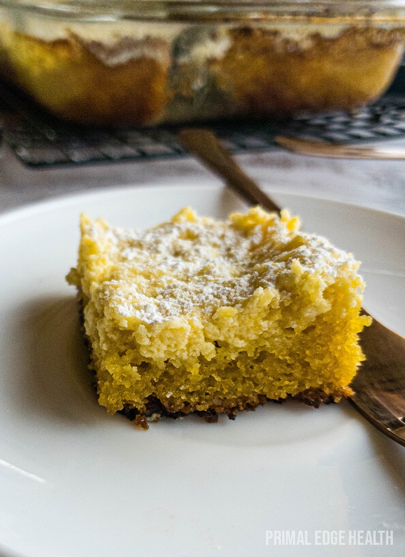 A piece of keto gooey butter cake on a white plate with a fork on the side.