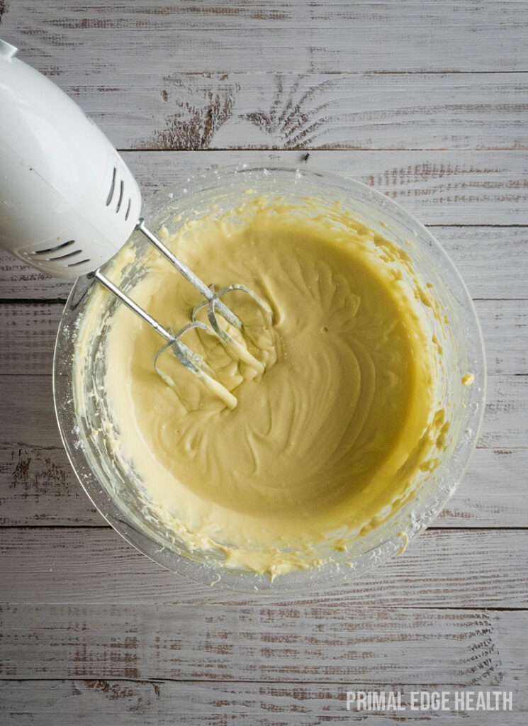 Electric mixer blending a creamy batter in a clear glass bowl.