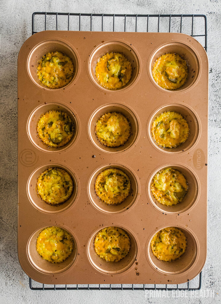 A dozen muffins in a brown muffin tray on a wire cooling rack.