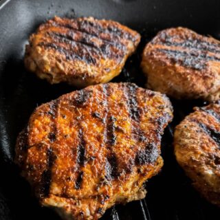 four blackened pork chops with grill marks in a cast iron skillet, two in full view, two cut off