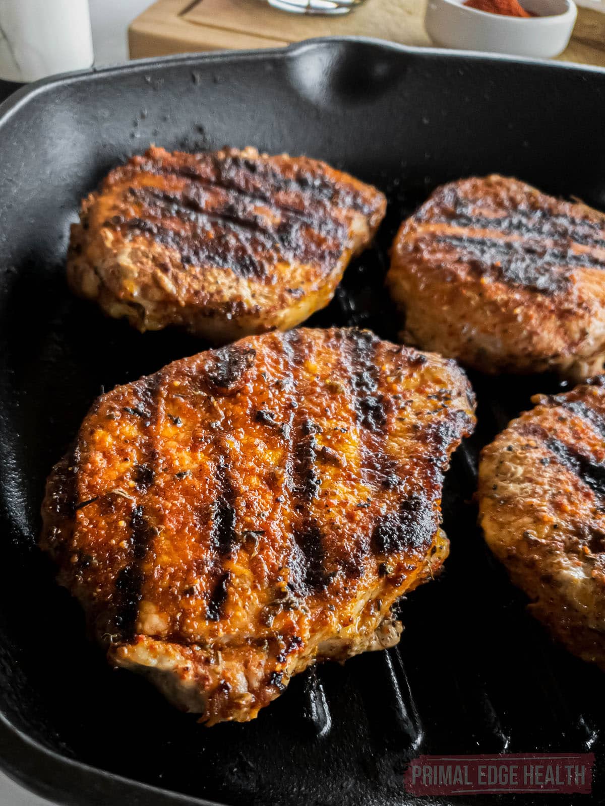 Four blackened pork chops with grill marks in a cast iron skillet.