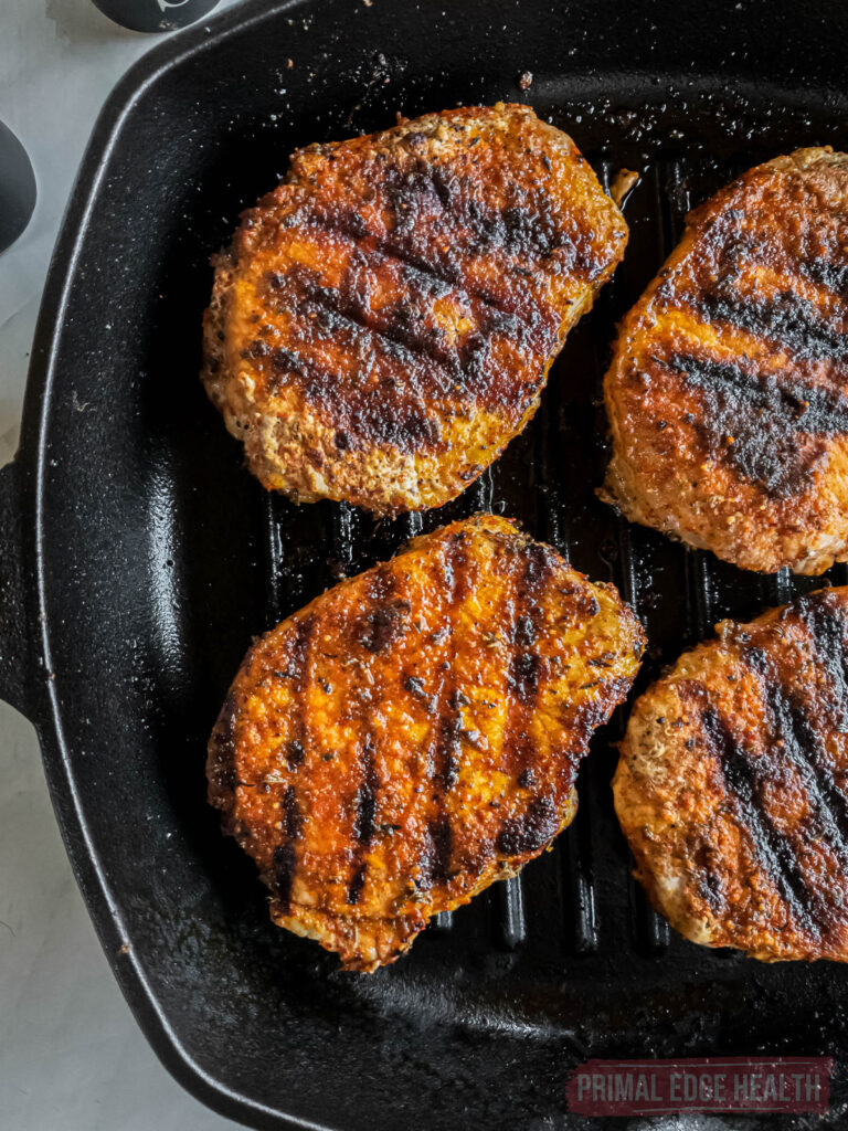 Three pork chops with sear marks cooking on a grill pan.