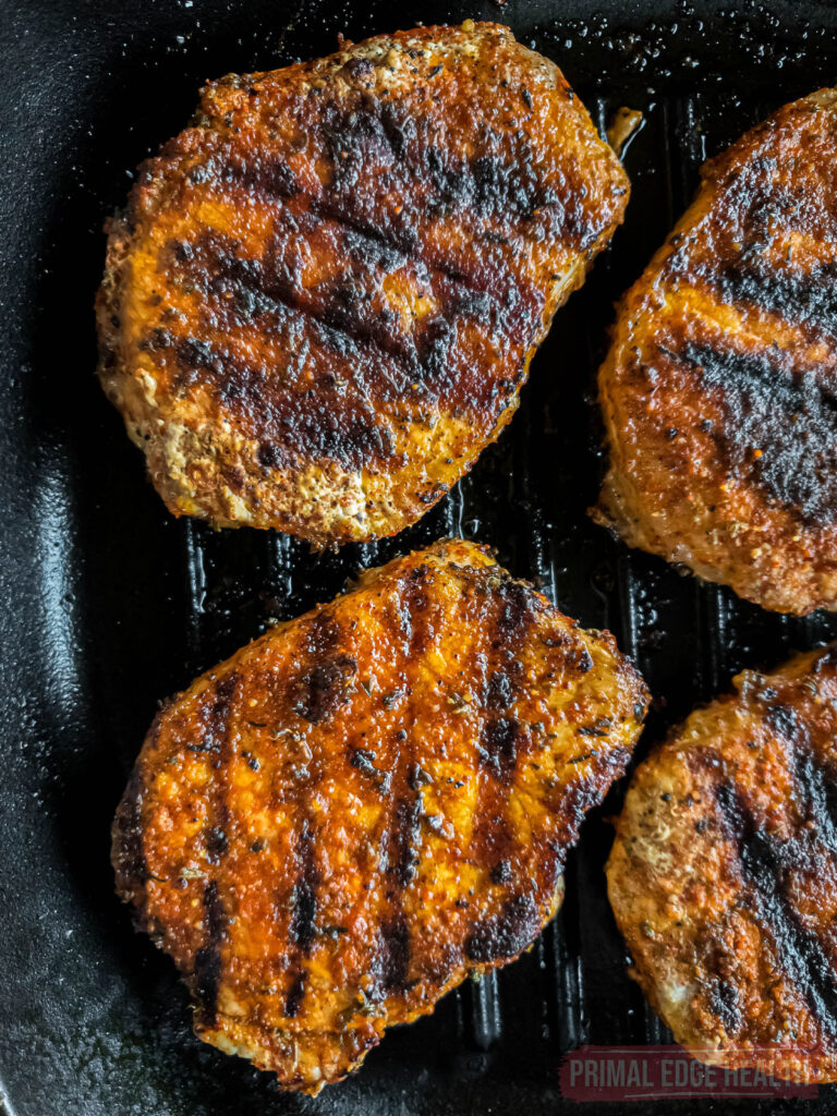 Three pork chops with char marks on a grill pan.