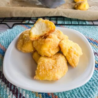 Cheese curds on white plate with bite out of one on a plate.