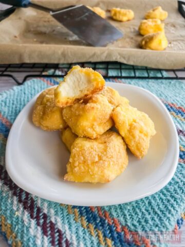 keto baked cheese curds on white plate with bite out of one and baking tray in the background