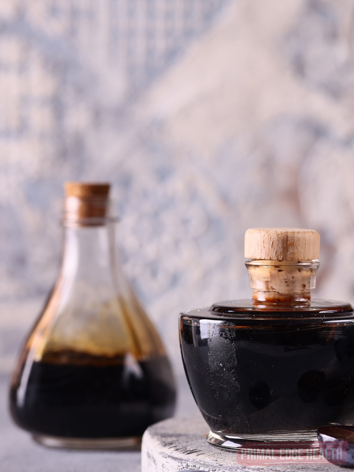 A glass jar with a cork stopper containing dark liquid, with a similar bottle blurred in the background.