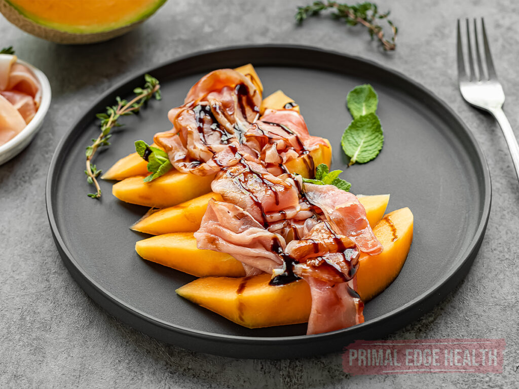 Sliced cantaloupe and prosciutto drizzled with black sauce on a plate.