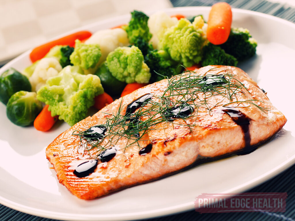A piece of salmon with vegetables on the side on a white plate.