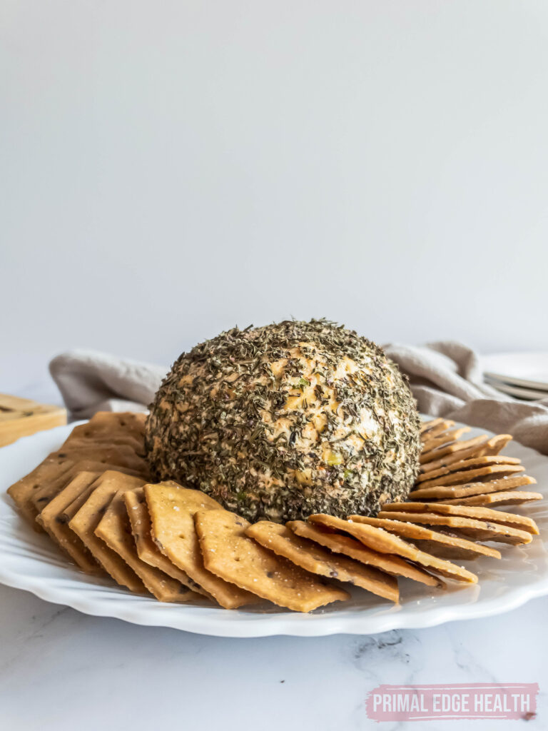 herb coated keto cheese ball on white serving plate surrounded by crackers