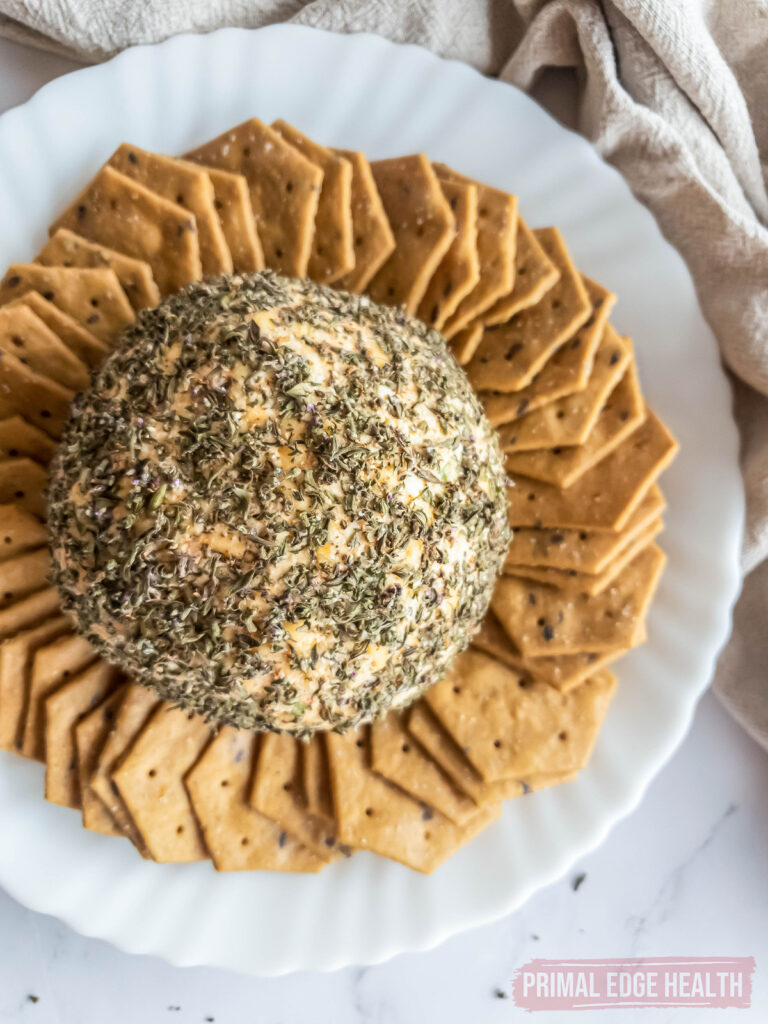 Cheese ball recipe coated with herbs, served with crackers on a plate.