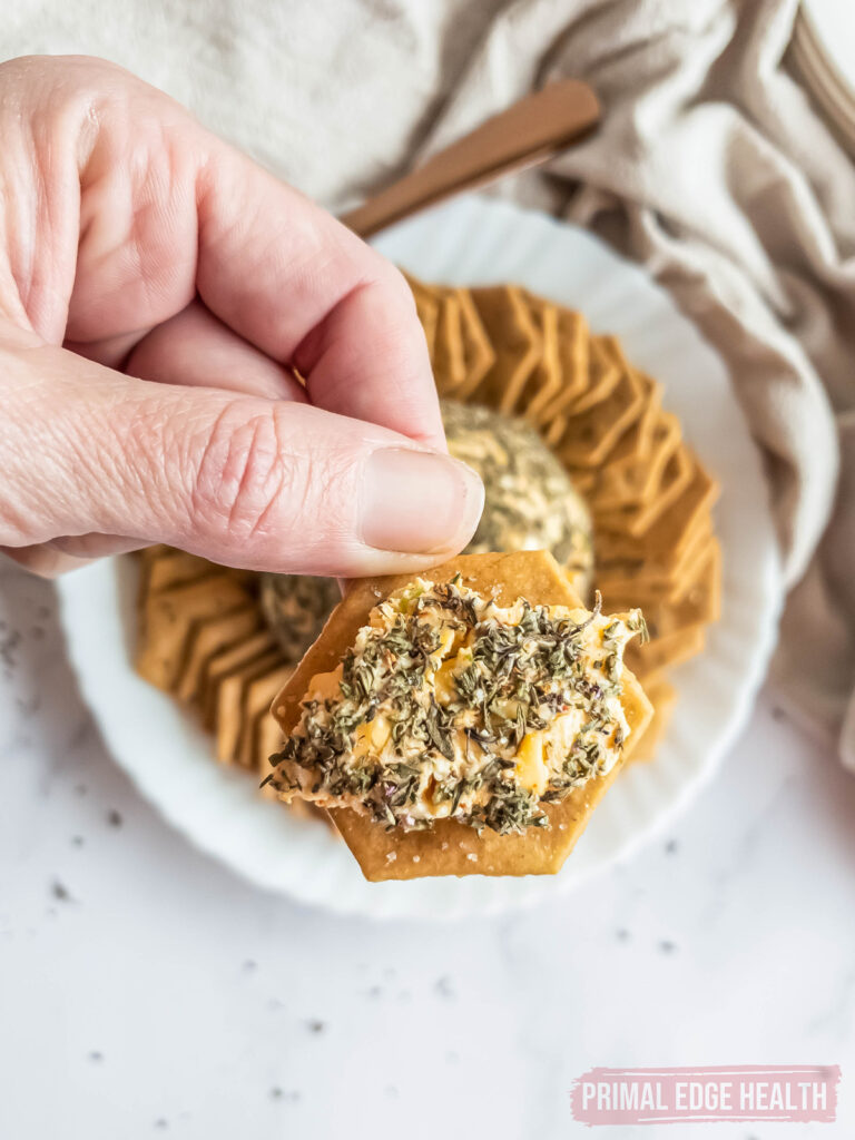 Hand holding a cracker with herb and cheese spread on top