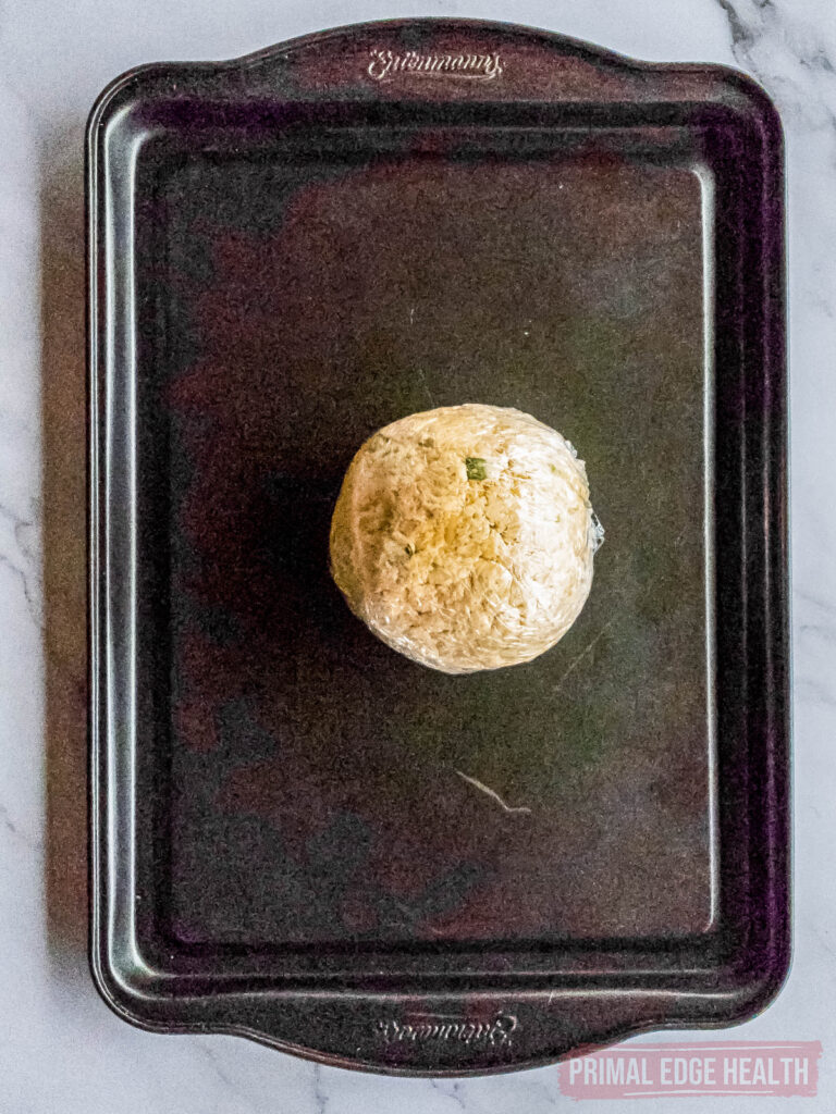 rolled cheese ball on baking sheet waiting for herb coating