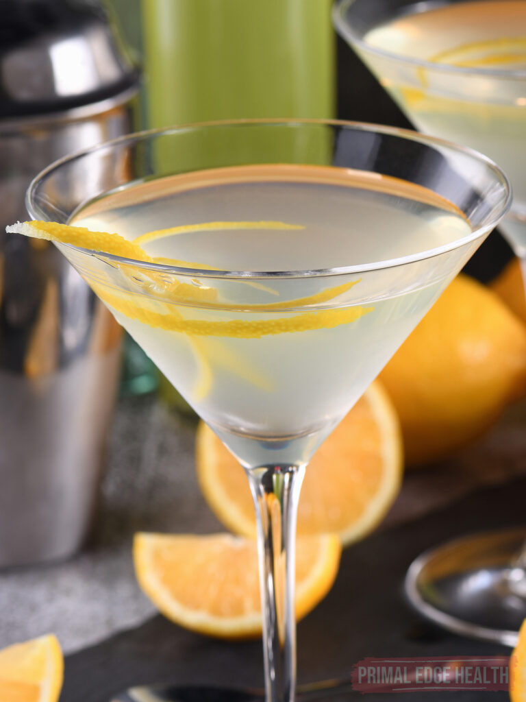 close up of low-carb lemon drop martini in a martini glass with lemon rind, shaker in the background