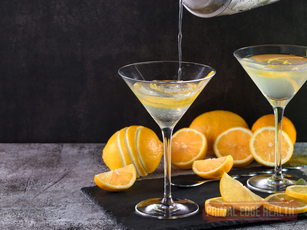 martini glass with a metal shaker pouring lemon drop martini into the glass and another glass full with lemon garnish