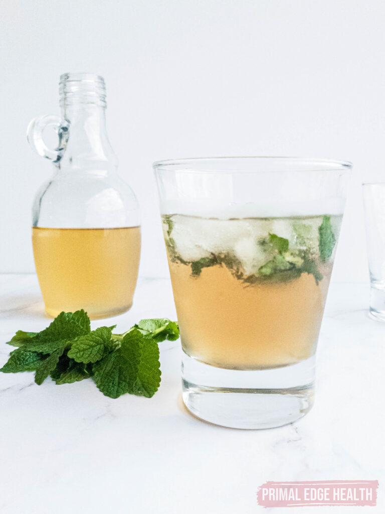 glass of keto mint julep over ice with fresh mint and bottle of bourbon alongside