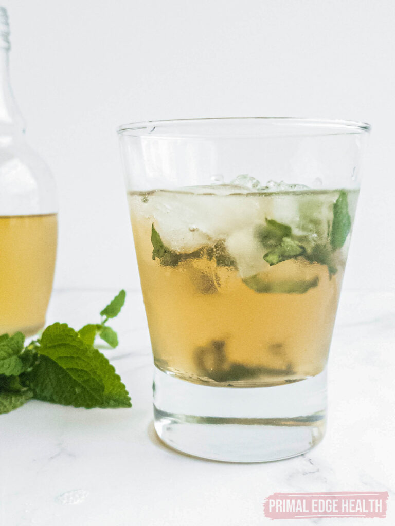 A glass of keto mint julep with mint leaves on a white surface.