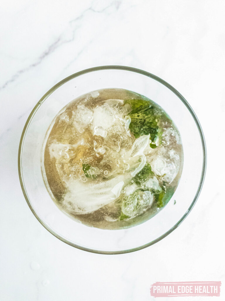 A glass containing a clear liquid with green leaves and ice cubes.