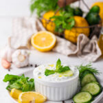 Bowl of keto tzatziki sauce garnished with herbs.