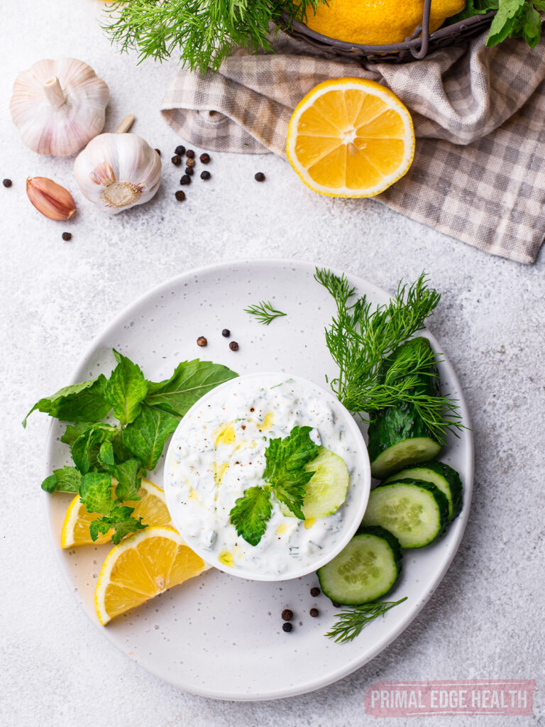 Easy tzatziki sauce in a bowl on a white plate with garnish and ingredients.